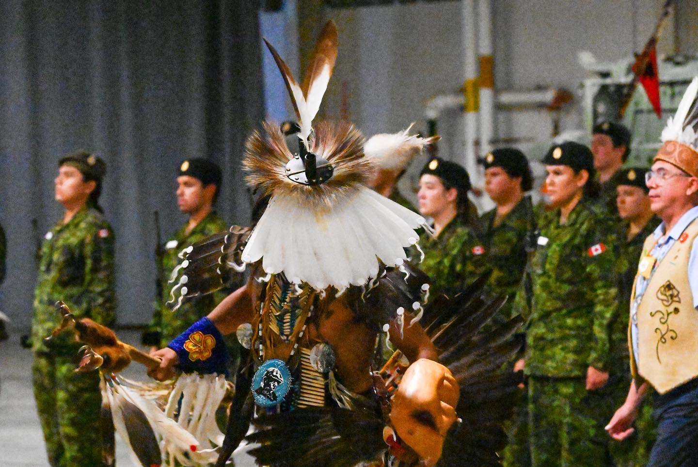 A dancer in regalia at a Black Bear ceremony, with Canadian Armed Forces participants standing behind