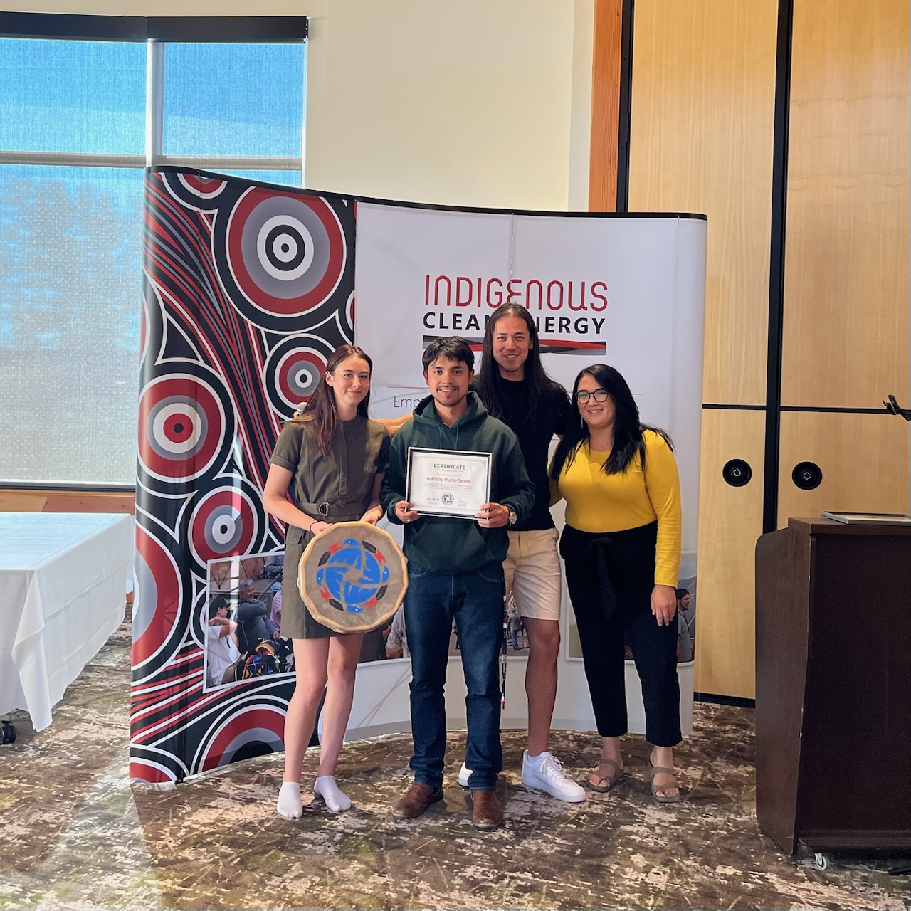 Anthony holding a certificate with fellow participants in front of an Indigenous Clean Energy backdrop
